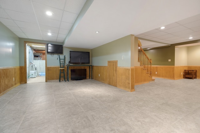 unfurnished living room featuring a drop ceiling and wood walls