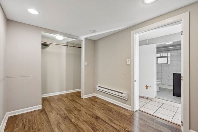 interior space with baseboard heating, a closet, tile walls, and hardwood / wood-style flooring