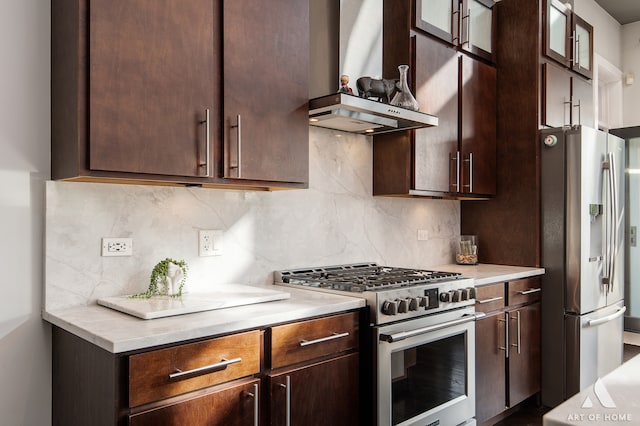 kitchen featuring wall chimney exhaust hood, dark brown cabinets, decorative backsplash, and stainless steel appliances