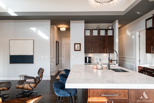 kitchen featuring a kitchen island with sink, sink, a notable chandelier, dark brown cabinets, and a breakfast bar area