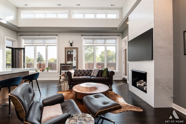 living room with a wealth of natural light, a fireplace, a towering ceiling, and dark hardwood / wood-style floors