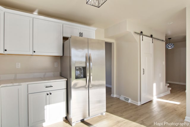 kitchen with a barn door, white cabinets, stainless steel refrigerator with ice dispenser, and light wood-type flooring