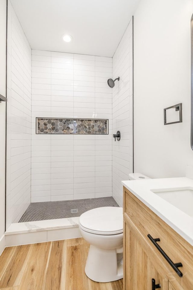 bathroom with hardwood / wood-style floors, vanity, a tile shower, and toilet