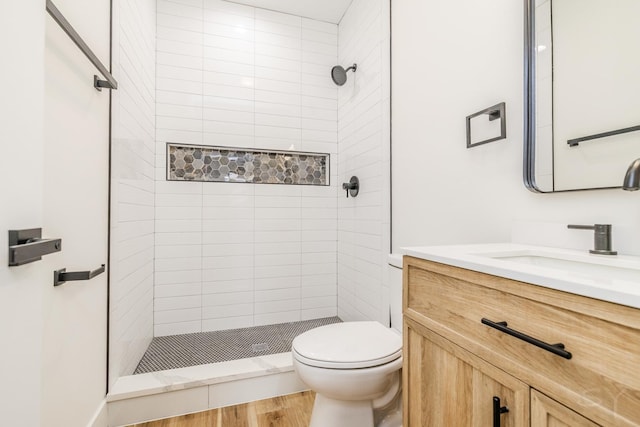 bathroom featuring vanity, toilet, wood-type flooring, and tiled shower