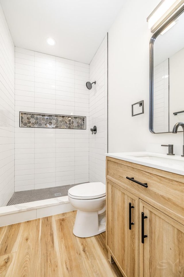 bathroom with tiled shower, hardwood / wood-style floors, vanity, and toilet