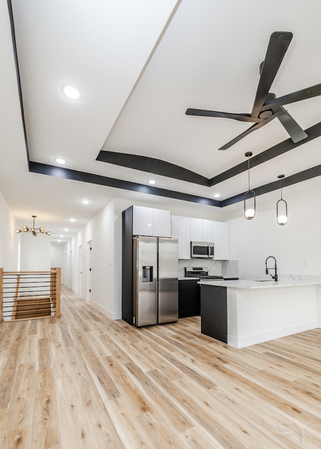 kitchen featuring a raised ceiling, hanging light fixtures, light hardwood / wood-style floors, white cabinetry, and stainless steel appliances