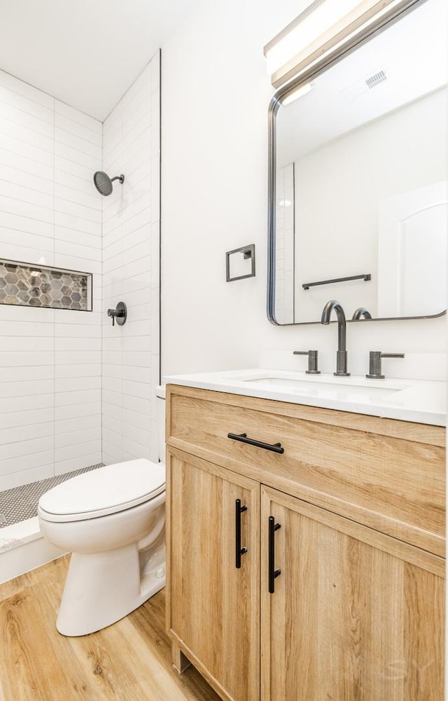 bathroom featuring hardwood / wood-style flooring, vanity, toilet, and a tile shower