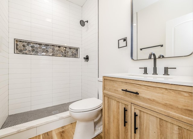 bathroom featuring a tile shower, vanity, hardwood / wood-style flooring, and toilet