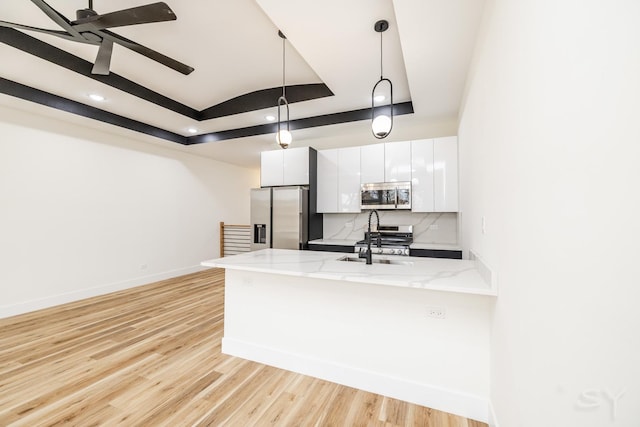 kitchen with white cabinets, appliances with stainless steel finishes, a tray ceiling, decorative light fixtures, and light hardwood / wood-style floors