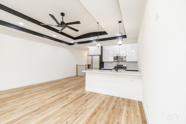 kitchen with pendant lighting, white cabinets, appliances with stainless steel finishes, a tray ceiling, and light hardwood / wood-style floors