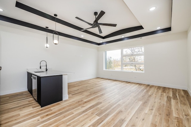 unfurnished living room featuring light wood-type flooring, a raised ceiling, ceiling fan, and sink