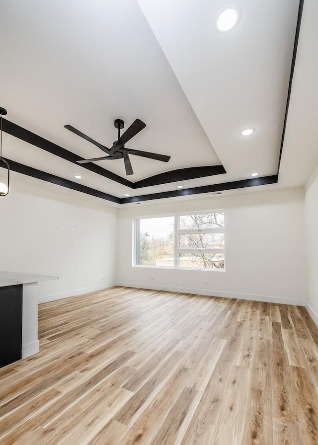 unfurnished living room featuring a raised ceiling, ceiling fan, and light hardwood / wood-style floors