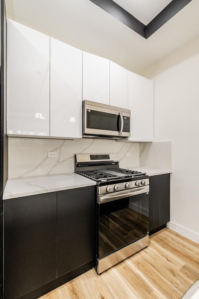 kitchen featuring decorative backsplash, white cabinets, light wood-type flooring, and appliances with stainless steel finishes