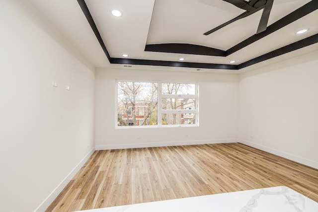 spare room featuring a raised ceiling, ceiling fan, and light hardwood / wood-style floors