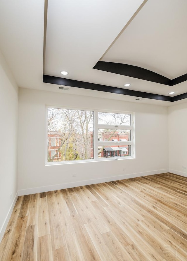 spare room with a tray ceiling and light hardwood / wood-style floors