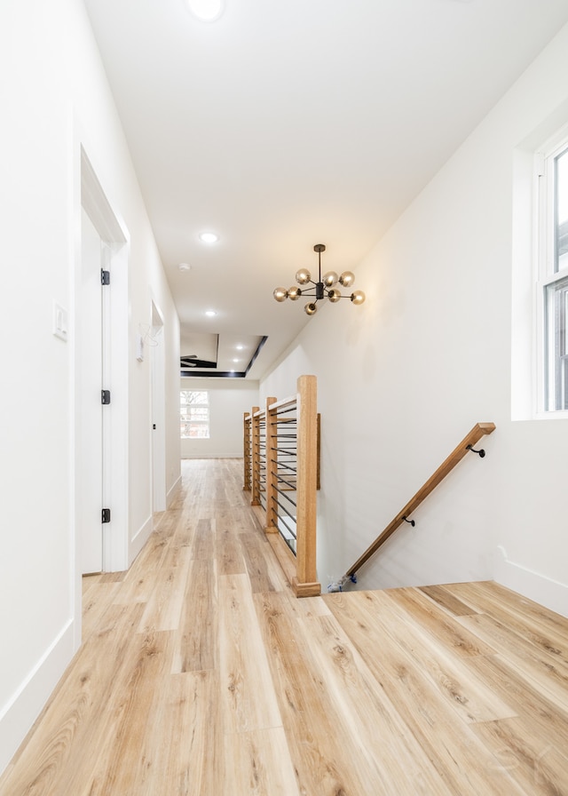 corridor featuring light wood-type flooring and an inviting chandelier