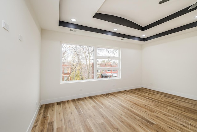 unfurnished room featuring light wood-type flooring and a raised ceiling