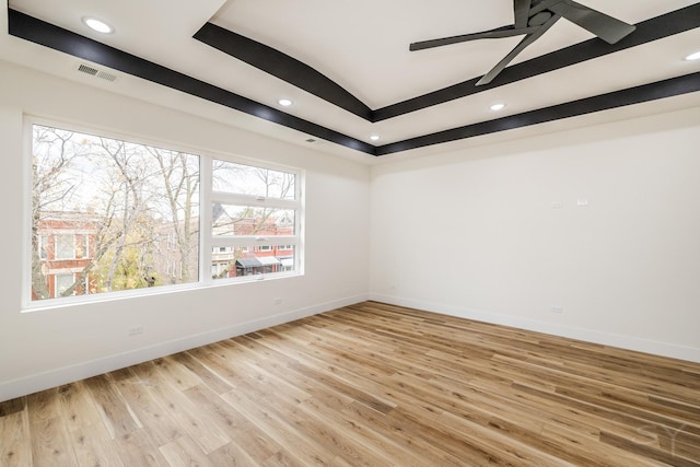 empty room with a raised ceiling, ceiling fan, and light hardwood / wood-style flooring