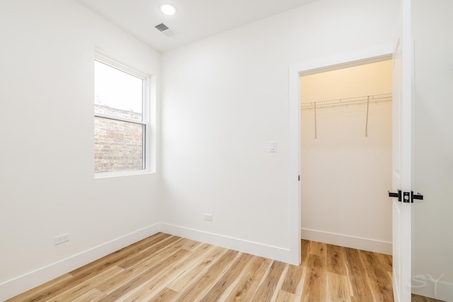 unfurnished bedroom featuring a spacious closet, a closet, and light hardwood / wood-style floors