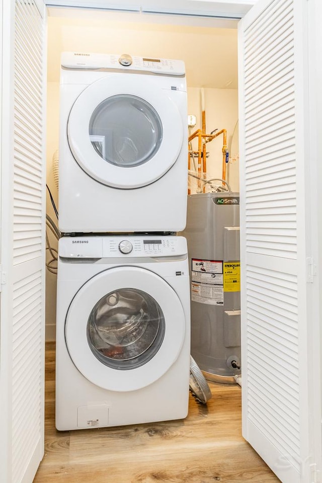 clothes washing area with hardwood / wood-style flooring, electric water heater, and stacked washer and clothes dryer