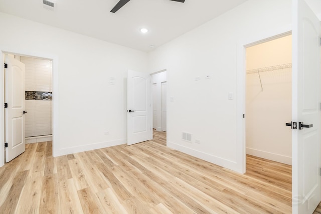 unfurnished bedroom featuring ceiling fan, a closet, a walk in closet, and light hardwood / wood-style flooring