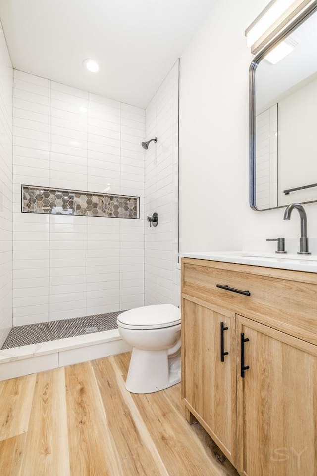 bathroom with tiled shower, vanity, wood-type flooring, and toilet