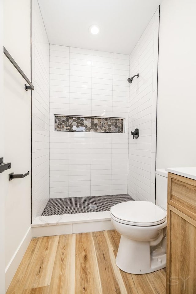 bathroom featuring vanity, toilet, wood-type flooring, and a tile shower