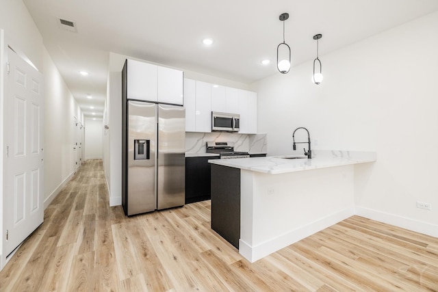 kitchen with appliances with stainless steel finishes, sink, decorative light fixtures, white cabinets, and light hardwood / wood-style floors