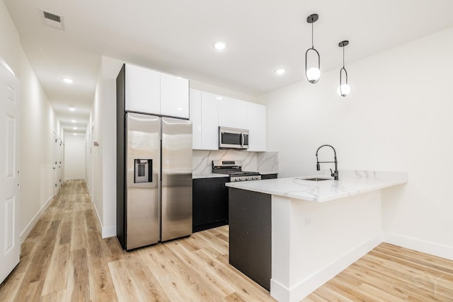 kitchen featuring sink, stainless steel appliances, pendant lighting, light hardwood / wood-style floors, and white cabinets