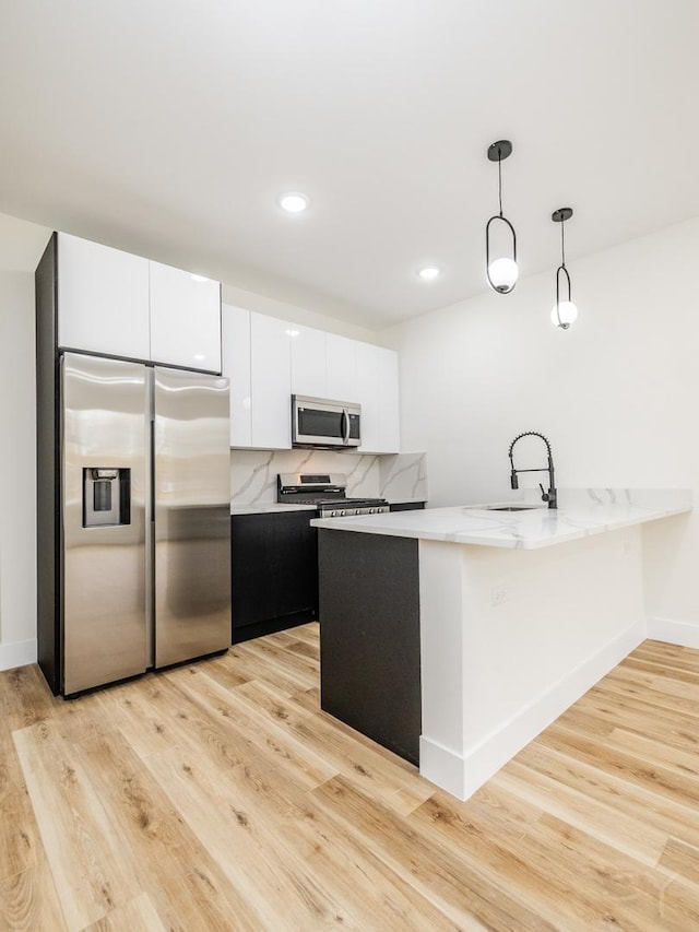 kitchen featuring stainless steel appliances, sink, pendant lighting, white cabinets, and light hardwood / wood-style floors