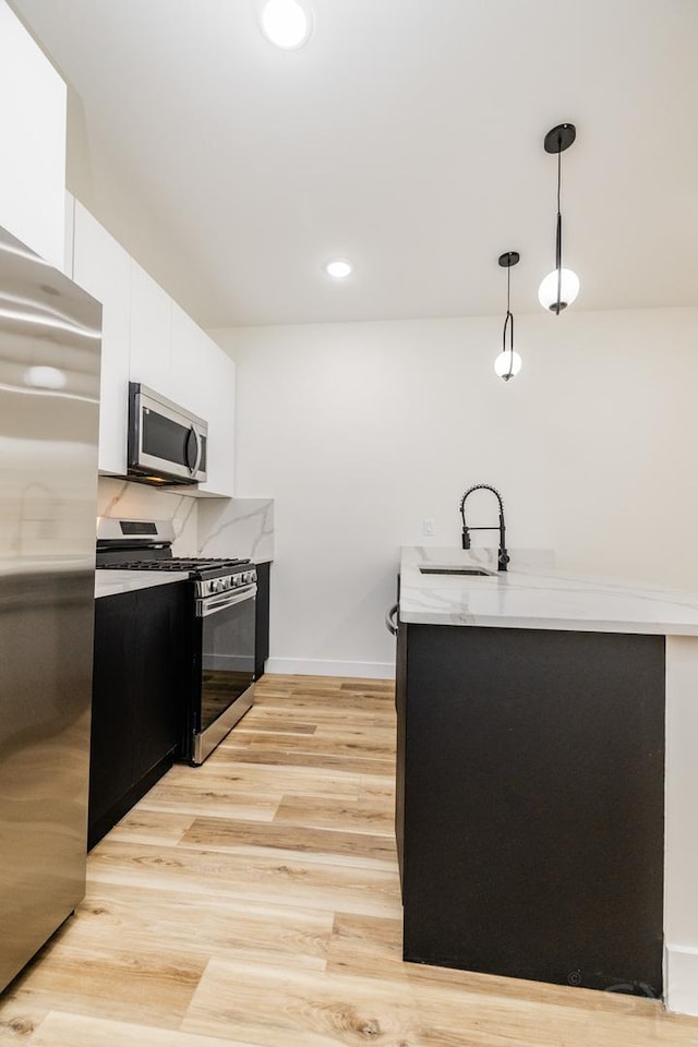 kitchen with pendant lighting, white cabinets, sink, light hardwood / wood-style flooring, and stainless steel appliances