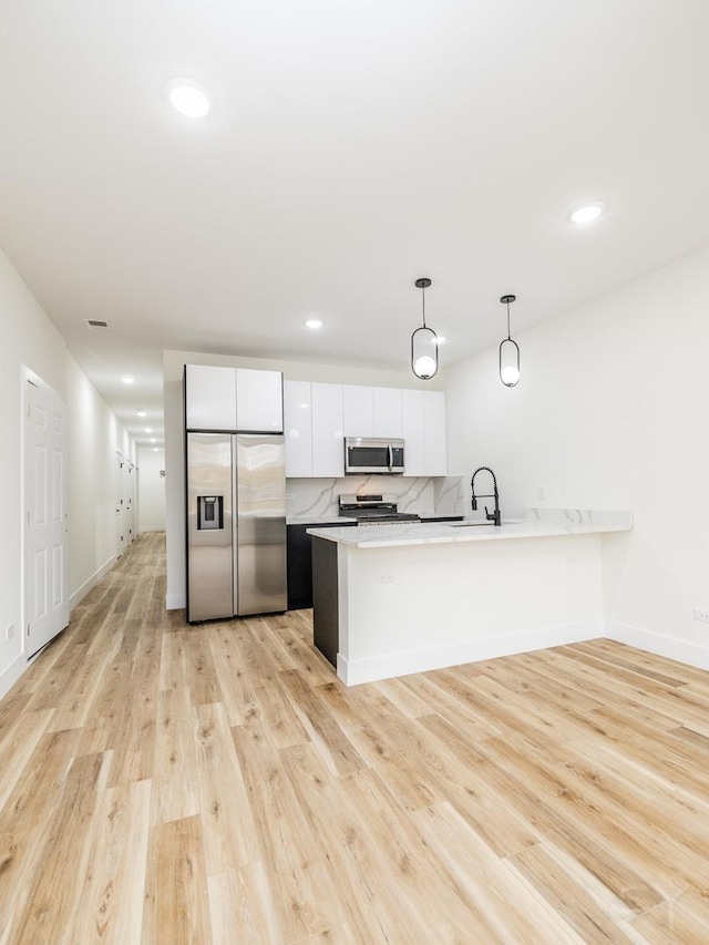 kitchen featuring white cabinetry, stainless steel appliances, hanging light fixtures, and light hardwood / wood-style flooring