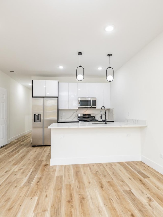 kitchen with pendant lighting, white cabinets, stainless steel appliances, and light hardwood / wood-style floors