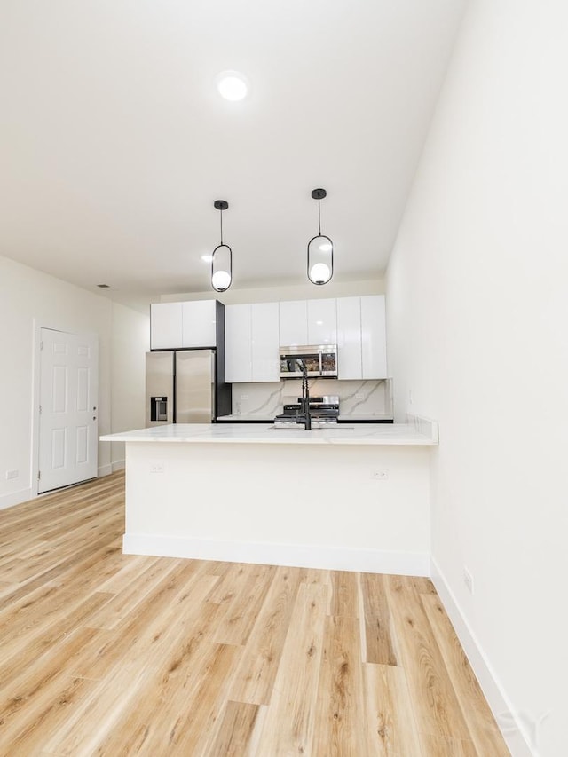 kitchen with kitchen peninsula, stainless steel appliances, light hardwood / wood-style flooring, white cabinets, and hanging light fixtures