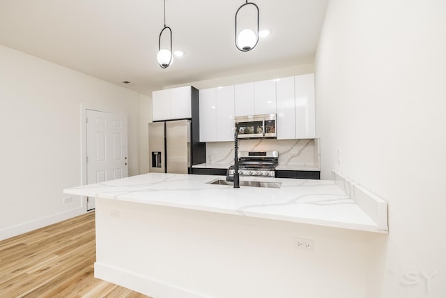 kitchen with kitchen peninsula, appliances with stainless steel finishes, light hardwood / wood-style flooring, white cabinets, and hanging light fixtures