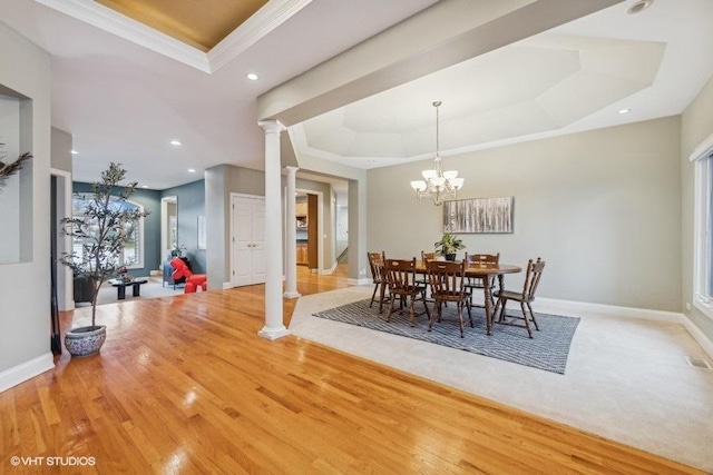 dining space featuring an inviting chandelier, decorative columns, light hardwood / wood-style flooring, and a tray ceiling