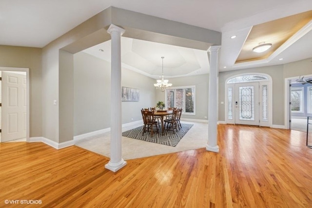 entrance foyer with a tray ceiling, decorative columns, a chandelier, and light wood-type flooring