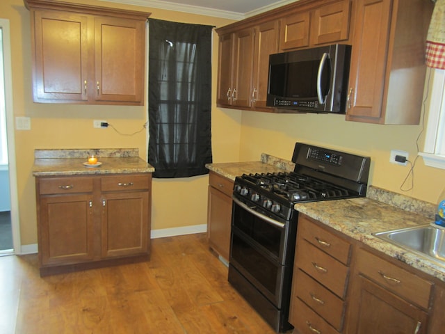 kitchen featuring sink, crown molding, light hardwood / wood-style flooring, black gas range oven, and light stone counters