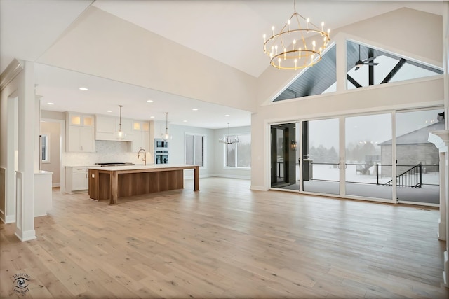 unfurnished living room with ceiling fan with notable chandelier, light wood-type flooring, and high vaulted ceiling