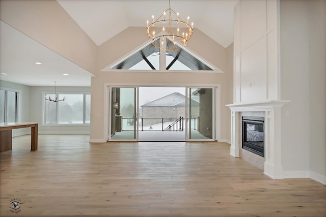 unfurnished living room featuring light wood-type flooring, high vaulted ceiling, and an inviting chandelier