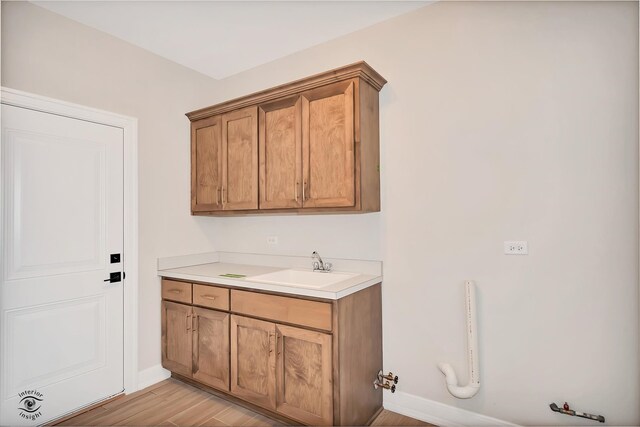 clothes washing area with sink, cabinets, and light wood-type flooring