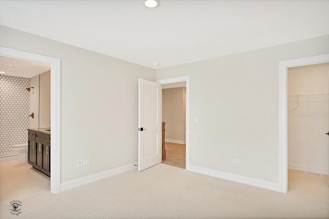 unfurnished bedroom featuring light carpet, a walk in closet, ensuite bath, and a closet