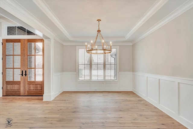 unfurnished dining area featuring a notable chandelier, ornamental molding, light hardwood / wood-style flooring, and french doors