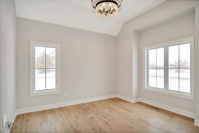 empty room with a chandelier, vaulted ceiling, and light wood-type flooring