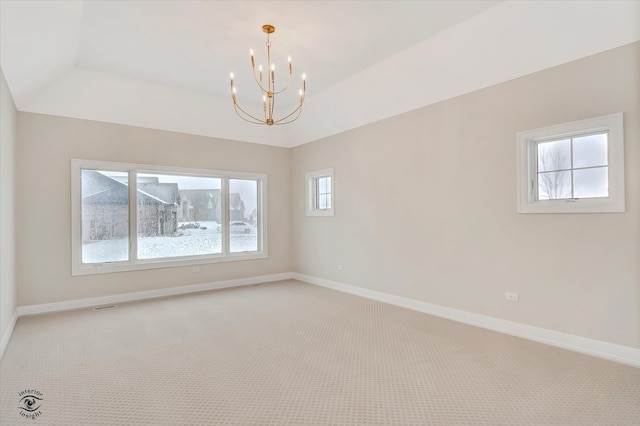 carpeted empty room featuring a raised ceiling, a wealth of natural light, and a notable chandelier