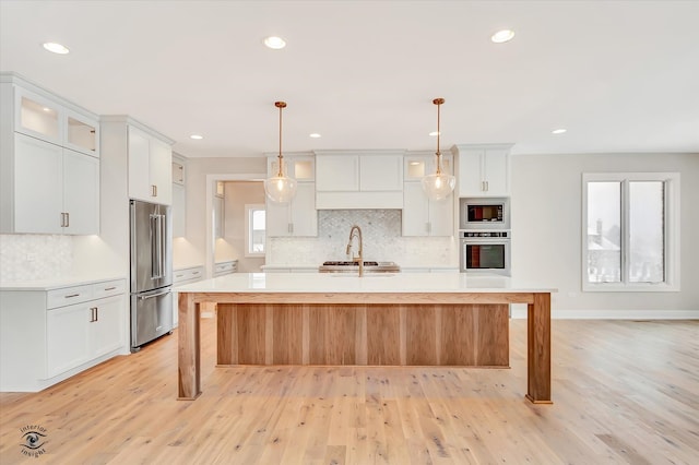 kitchen with decorative light fixtures, light wood-type flooring, stainless steel appliances, and an island with sink