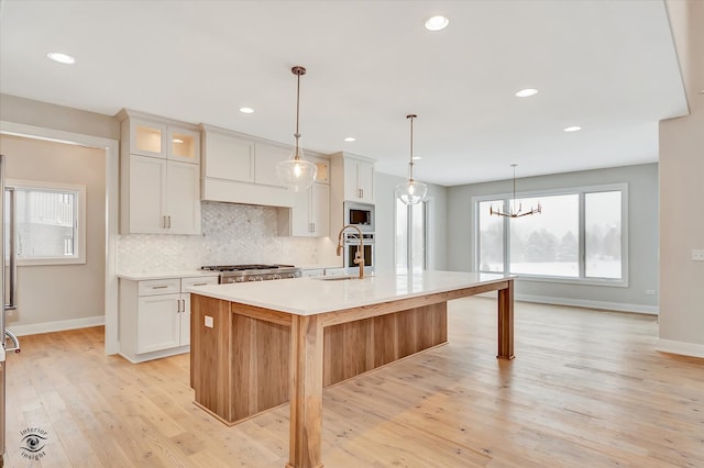 kitchen featuring appliances with stainless steel finishes, sink, white cabinets, light hardwood / wood-style floors, and an island with sink