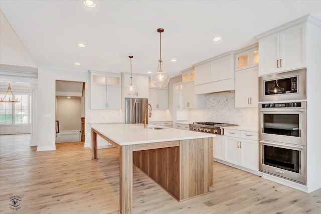 kitchen featuring pendant lighting, a center island with sink, white cabinets, light hardwood / wood-style flooring, and appliances with stainless steel finishes