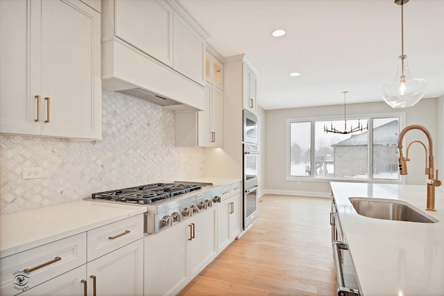 kitchen with pendant lighting, white cabinets, sink, light hardwood / wood-style flooring, and appliances with stainless steel finishes