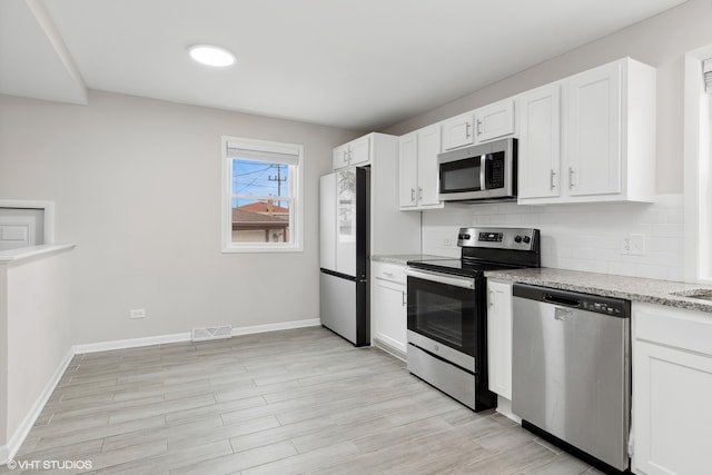 kitchen with white cabinets, backsplash, light stone counters, and stainless steel appliances